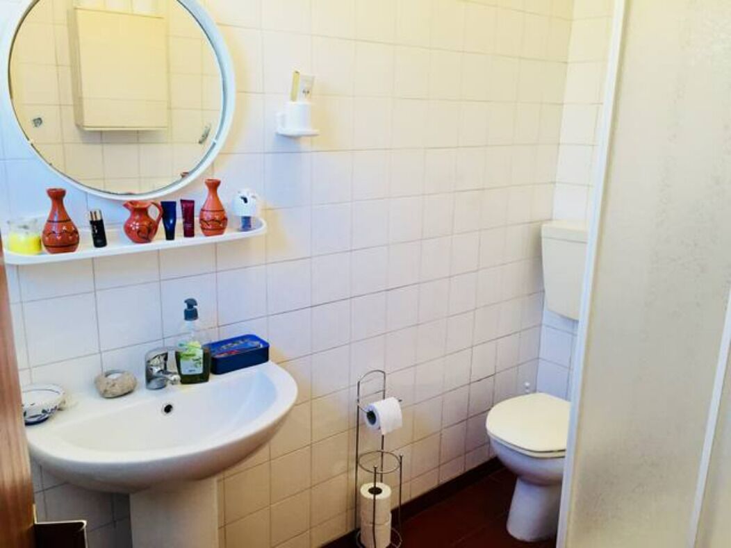 A bathroom with a sink, mirror, toilet, and shelves with toiletries.