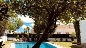 Une piscine entourée d’une cour verdoyante, avec un arbre au premier plan.
