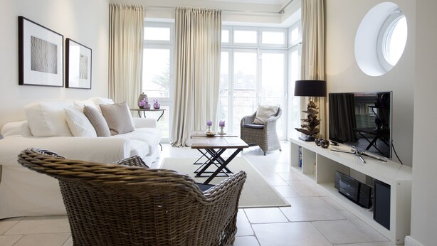 En moderne stue med en hvid sofa, en fletstol, et fjernsyn og en pejs.