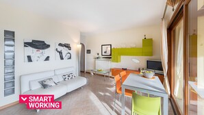 Un salon moderne avec un canapé blanc, une table  à manger et des chaises, ainsi que des œuvres d’art accrochées aux murs.