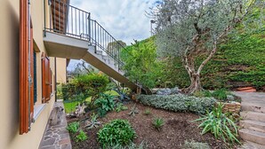 Un jardin avec un chemin de pierre, une terrasse en bois et un escalier menant à un balcon.