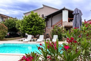 A swimming pool with white lounge chairs, a covered patio area, and a stone wall.