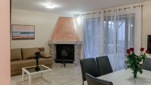 Un salon avec une cheminée, un canapé, une table basse et un coin repas comprenant des chaises et un vase de fleurs.