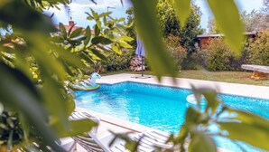 Une piscine à l’eau d’un bleu cristallin, entourée de verdure et dotée d’une terrasse en bois.