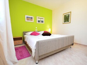 A bedroom with a bed, a nightstand, a pink rug, and two framed pictures on the wall.