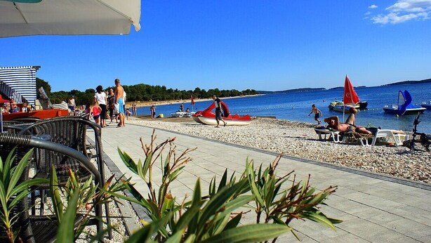 Une zone de plage bordée d’une rangée de chaises de plage et de parasols, avec un petit bateau et quelques personnes qui se promènent.