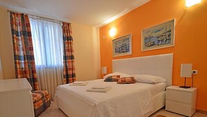 Une chambre à coucher avec un grand lit, une table de chevet, une lampe et une fenêtre avec des rideaux.