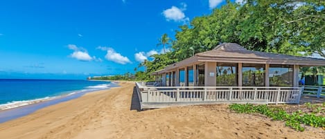 Uma praia com um pavilhão coberto, areal e vista para o oceano.