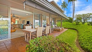 Una casa moderna con un porche cubierto, puertas correderas de cristal que dan a una cocina y un jardín exuberante con palmeras.