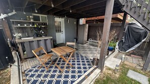 Un patio couvert avec une table et des chaises en bois, un tapis à motifs et un petit jardin agrémenté de plantes en pot.