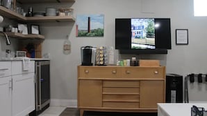 Une cuisine moderne avec des meubles blancs, un meuble en bois, un téléviseur fixé au mur et une fenêtre donnant sur un immeuble.