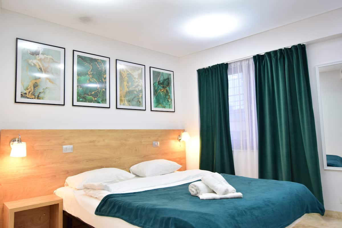 Ein Hotelzimmer mit einem Bett, zwei Wandleuchten, einem Holz-Kopfteil und drei gerahmten Kunstwerken an der Wand.