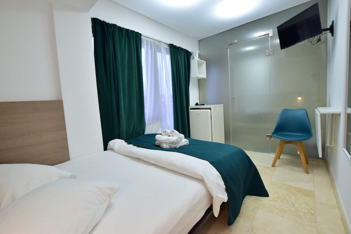 Ein Hotelzimmer mit Bett, Schreibtisch, Stuhl, Fernseher und einer Dusche.