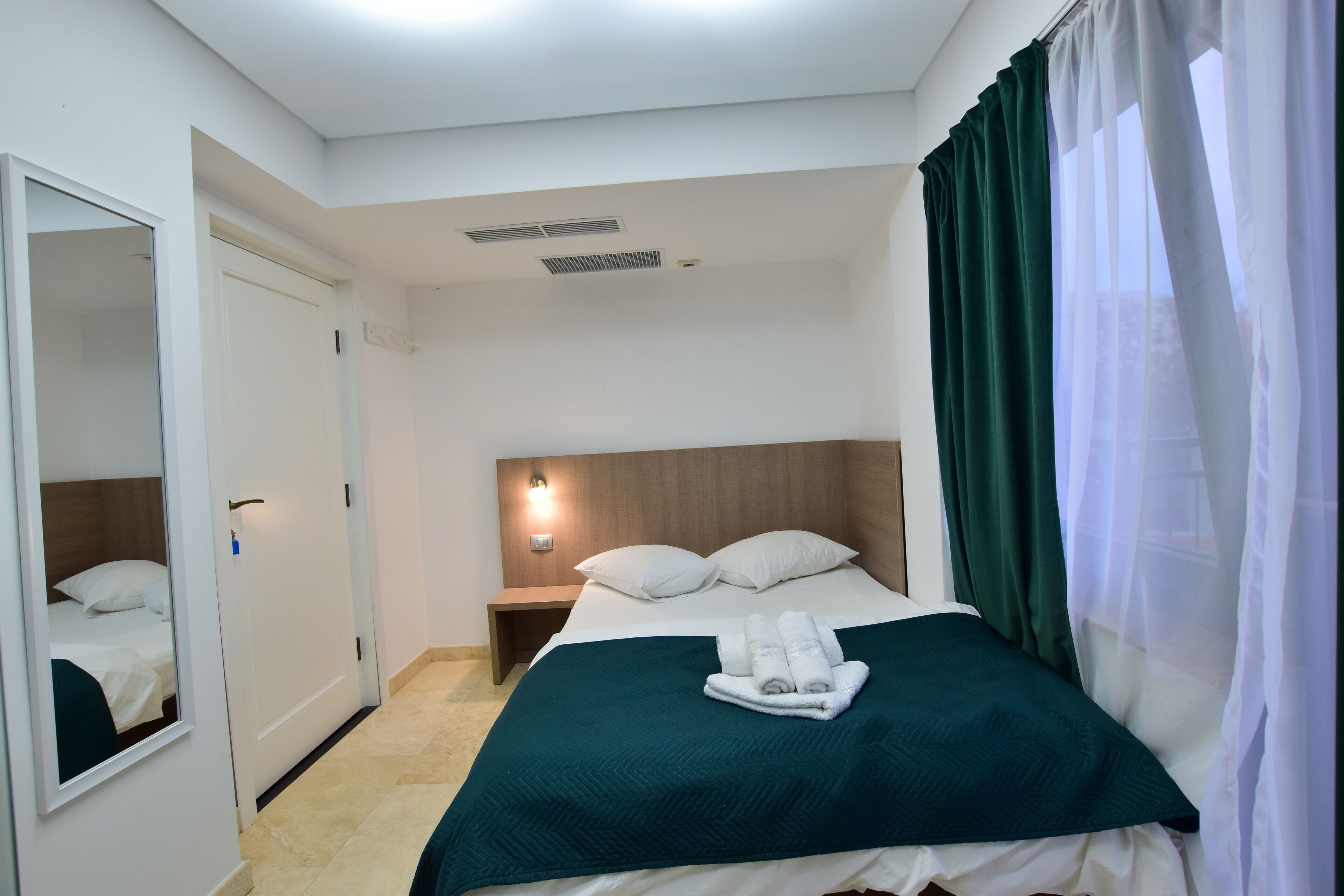 Una habitación de hotel con cama, mesita de noche, espejo y ventana con cortinas.