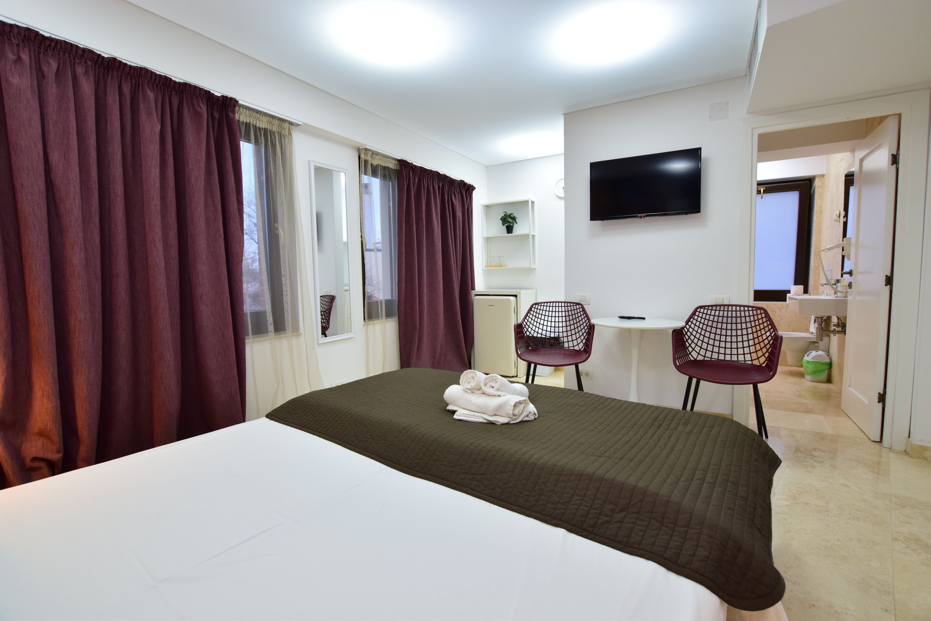 Une chambre d’hôtel avec un lit, deux chaises, une télévision, un bureau et une salle de bain visible à travers une porte ouverte.