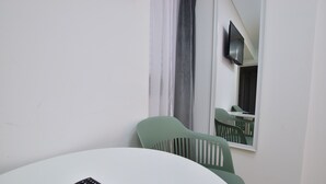 A room with a white round table, a green chair, and a black remote control. - Dacia Residence Apartments (Bucharest)