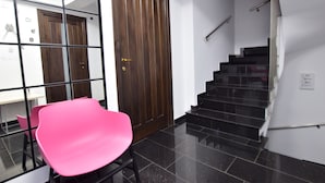A staircase with black steps and a handrail, a wooden door with a brass handle, and a pink chair in front of a glass partition. - Dacia Residence Apartments (Bucharest)