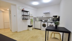 A compact kitchen with a washing machine, microwave, and a small dining area with a chair. - Dacia Residence Apartments (Bucharest)