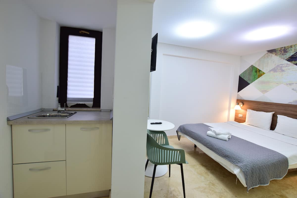Ein kleines Hotelzimmer mit Küchenzeile, einem Einzelbett, einem Tisch und einem Stuhl.