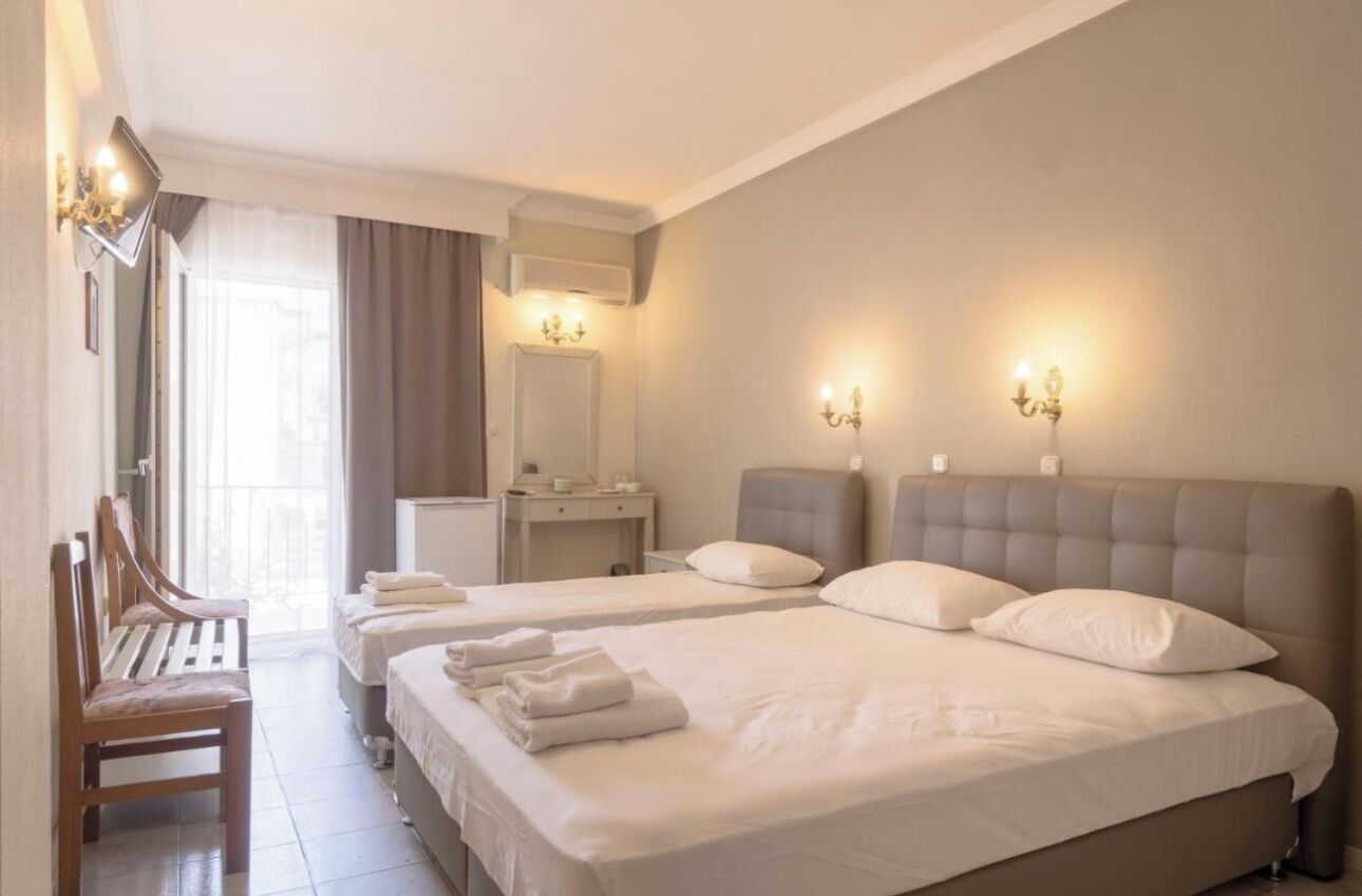Quarto de hotel com duas camas, área de estar com um banco, penteadeira com espelho e iluminação embutida na parede.