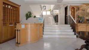 Et hotel lobby med receptionsskranke, trappe og et opholdsområde med træskabe og planter.