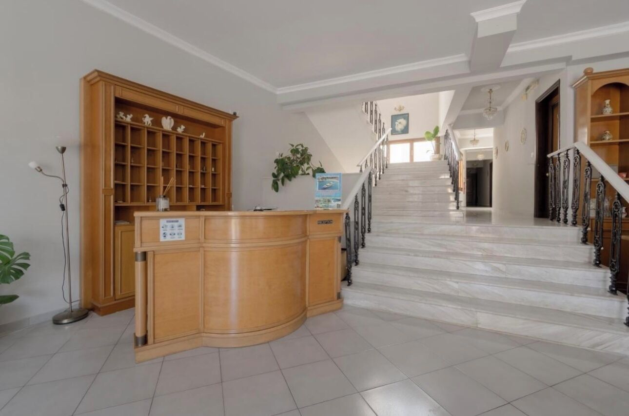 Un área de recepción con un escritorio de madera, una planta y una escalera que sube a otro piso.