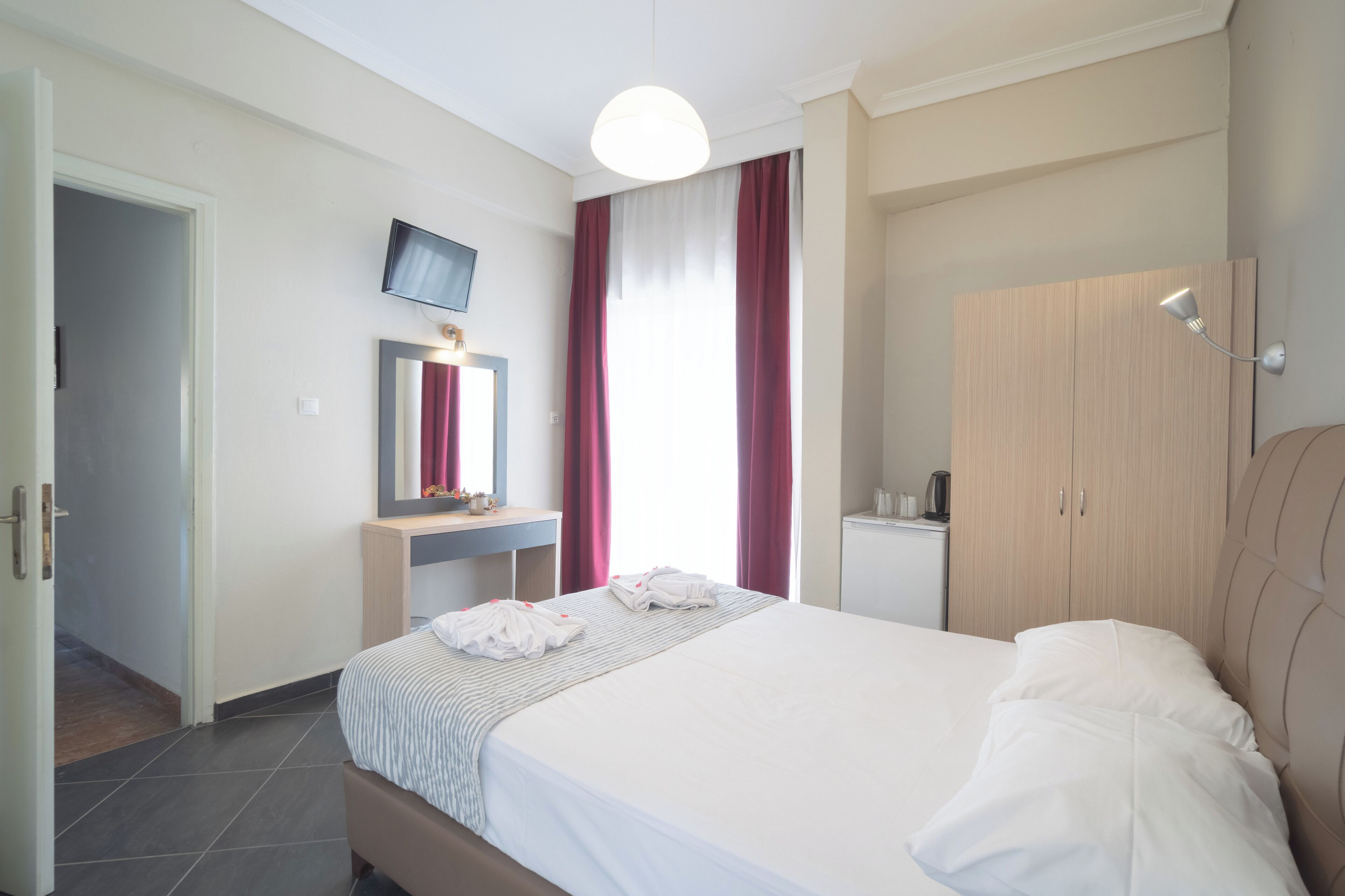 Habitació d'hotel amb llit, escriptori, televisió, armari i mirall.
