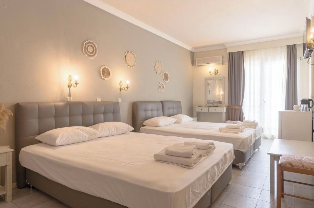 A hotel room with two beds, a desk, a chair, and a TV.