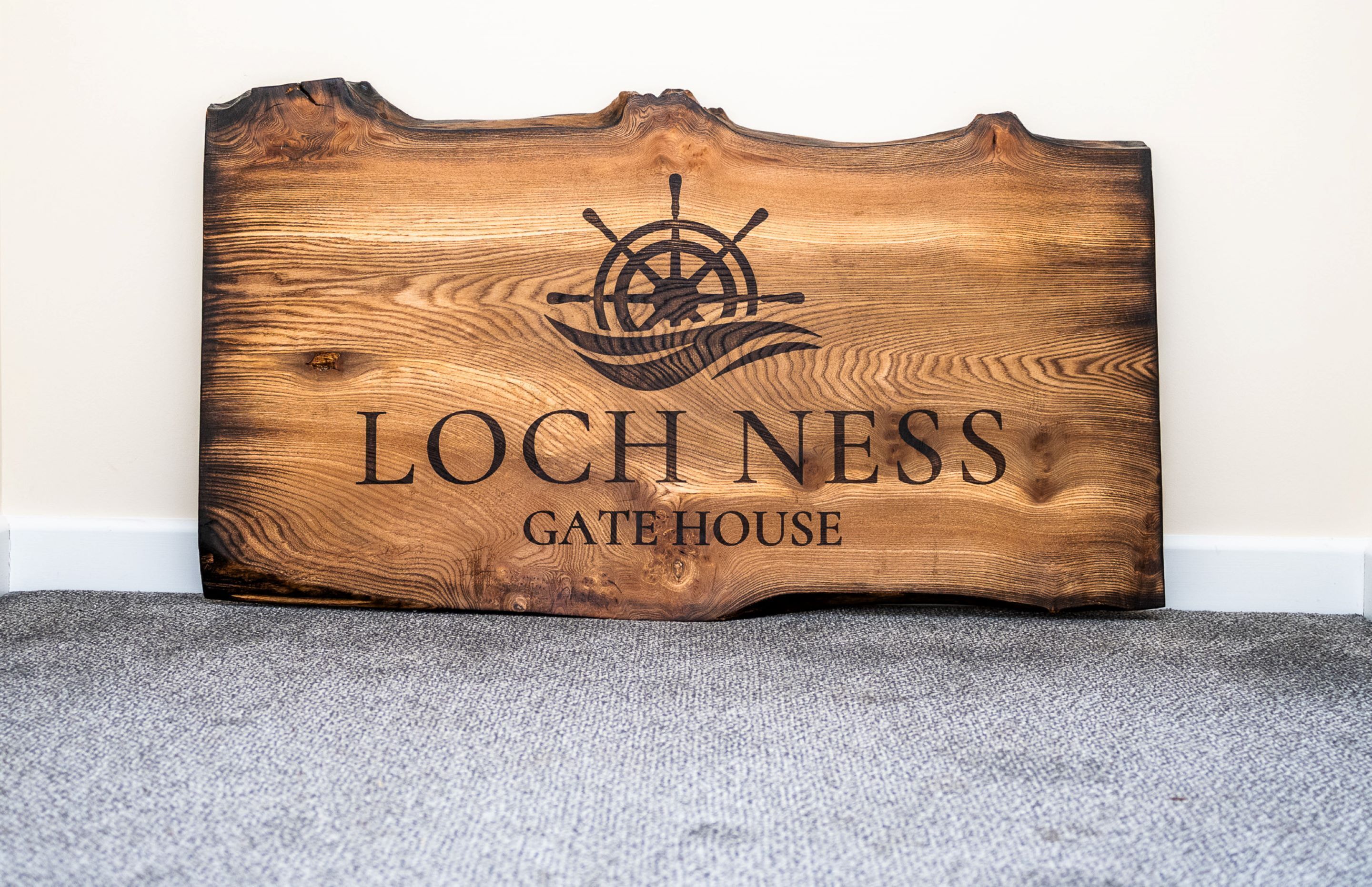 Et træskilt med et skibsråd og teksten "LOCHNESS GATE HOUSE".