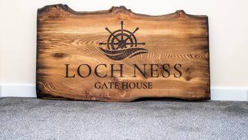 Un letrero de madera con un timón de barco y el texto 'LOCHNESS GATE HOUSE'.