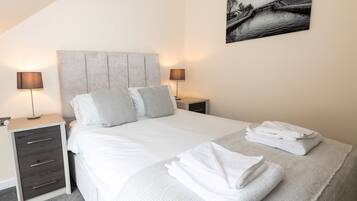 Una cama bien hecha con almohadas, una lámpara de noche, una toalla doblada y un cuadro en la pared.