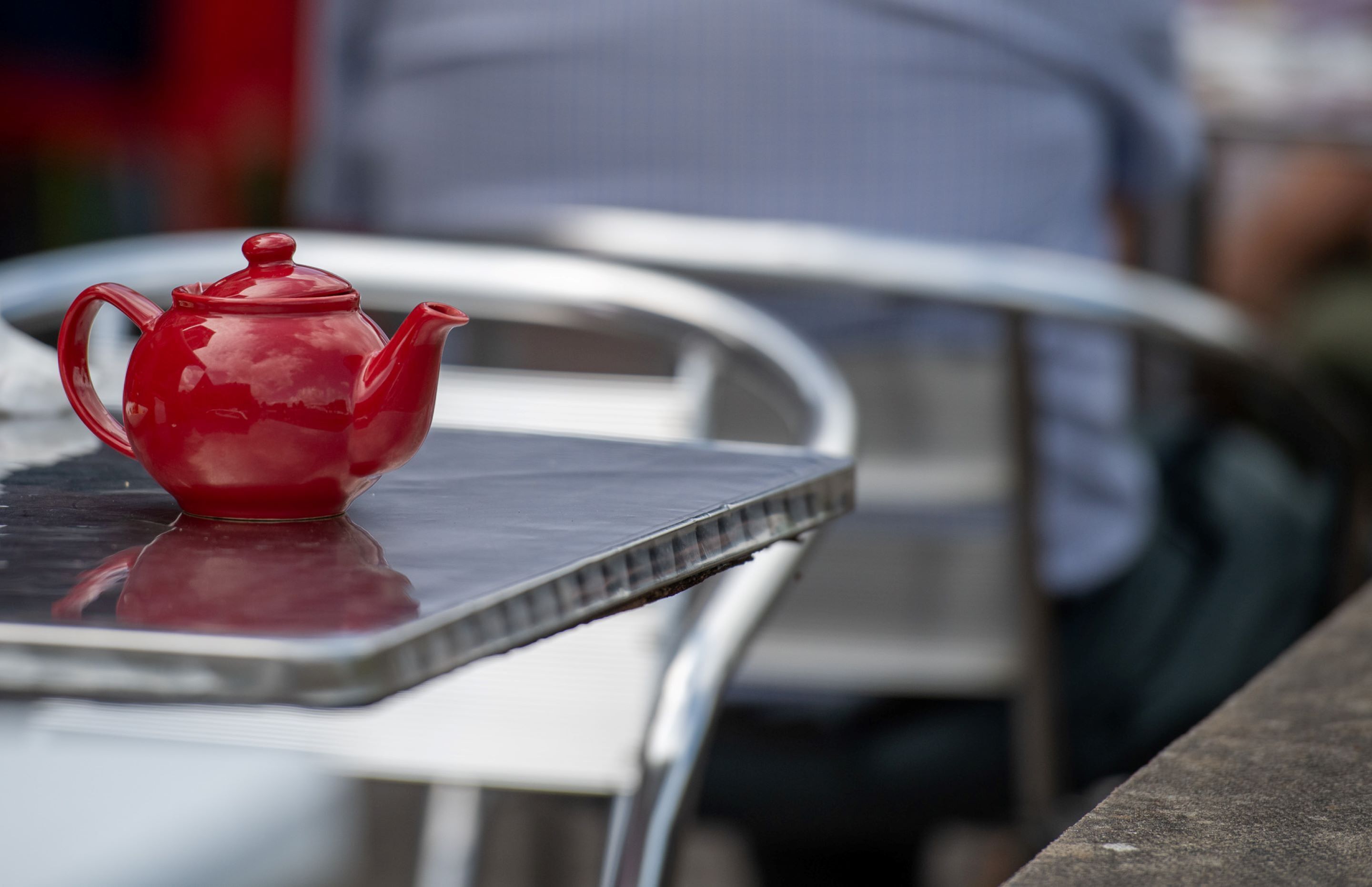 A red teapot on a metal table with a reflective surface.