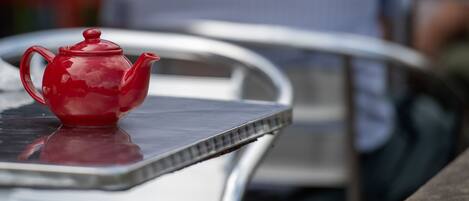 A red teapot on a metal table with a reflective surface.