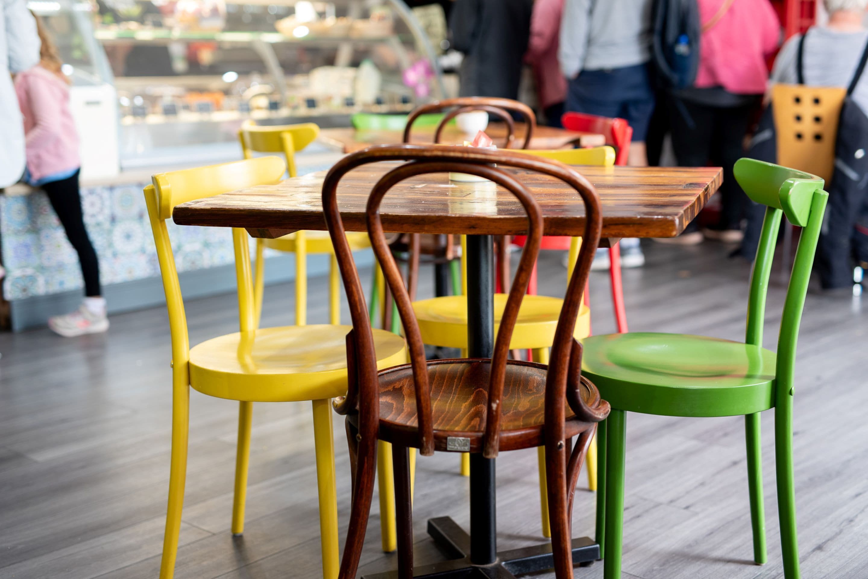 A restaurant interior with wooden tables and chairs, a tiled floor, and a counter with a display case.