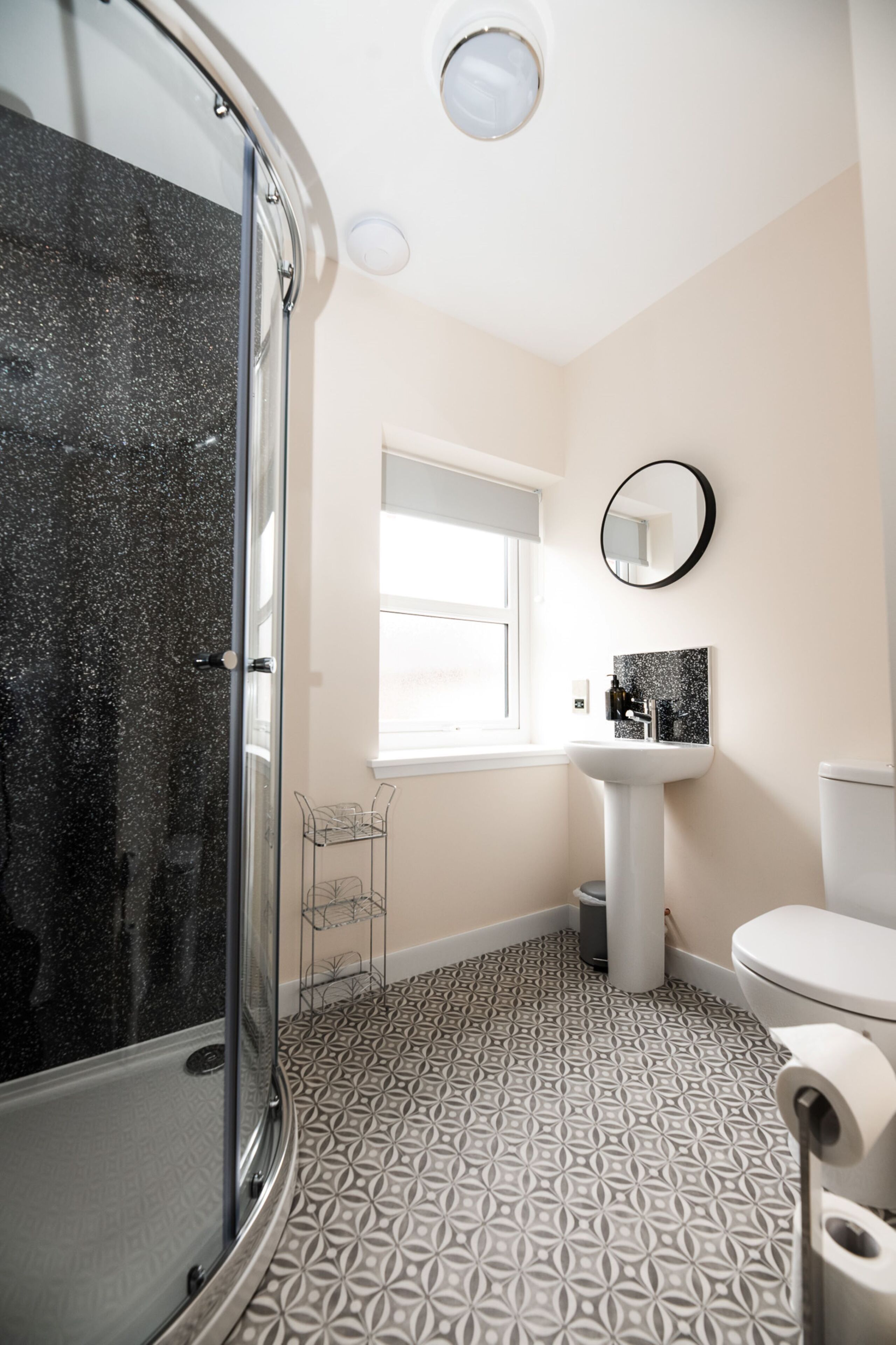 A bathroom with a shower, sink, toilet, and a window.