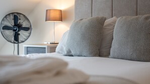 A neatly made bed with a headboard, a bedside fan, and a lamp on a nightstand. - Loch Ness Gate House (Fort Augustus)
