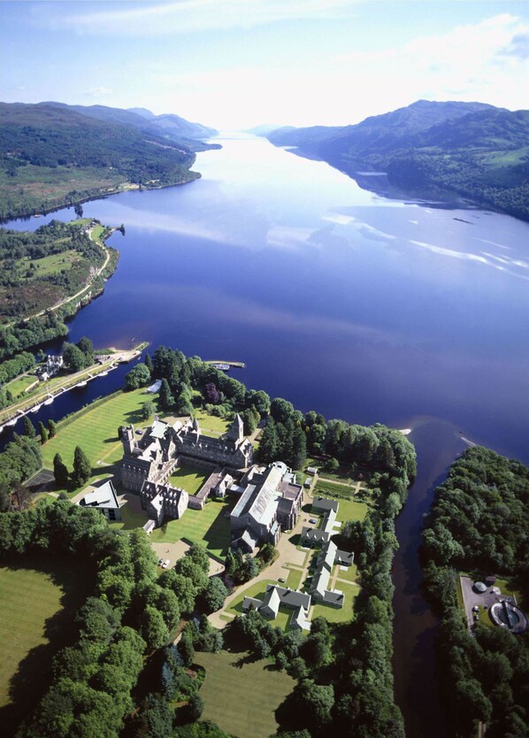 An aerial view of a historic estate with multiple buildings, a large lake, and surrounding greenery.
