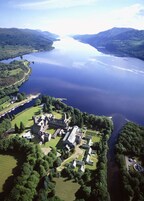 An aerial view of a historic estate with multiple buildings, a large lake, and surrounding greenery.