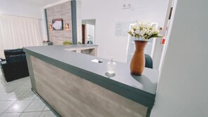 Un comptoir d’accueil orné d’un vase de fleurs, muni d’un distributeur de gel hydroalcoolique et d’une signalétique fixée au mur.
