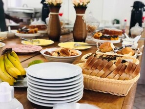 Une table de buffet garnie de divers aliments, notamment du pain, des pâtisseries et une pile d’assiettes.
