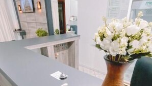 A reception desk with a vase of white flowers, a hand sanitizer dispenser, and a framed picture on the wall. - Nacional Park Hotel Lages (Lages)