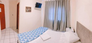 Une chambre à coucher avec un lit, une table de chevet, une télévision et une fenêtre avec des rideaux.