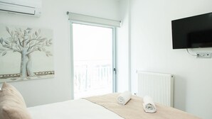 A hotel room with a bed, a painting of a tree, a TV mounted on the wall, and a window with a view of a balcony. - Cozy and spacious apartment in Zografou (Zografos)