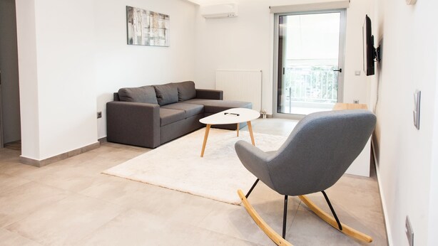 A modern living room with a grey sofa, a white coffee table, and a rocking chair. - Cozy and spacious apartment in Zografou (Zografos)
