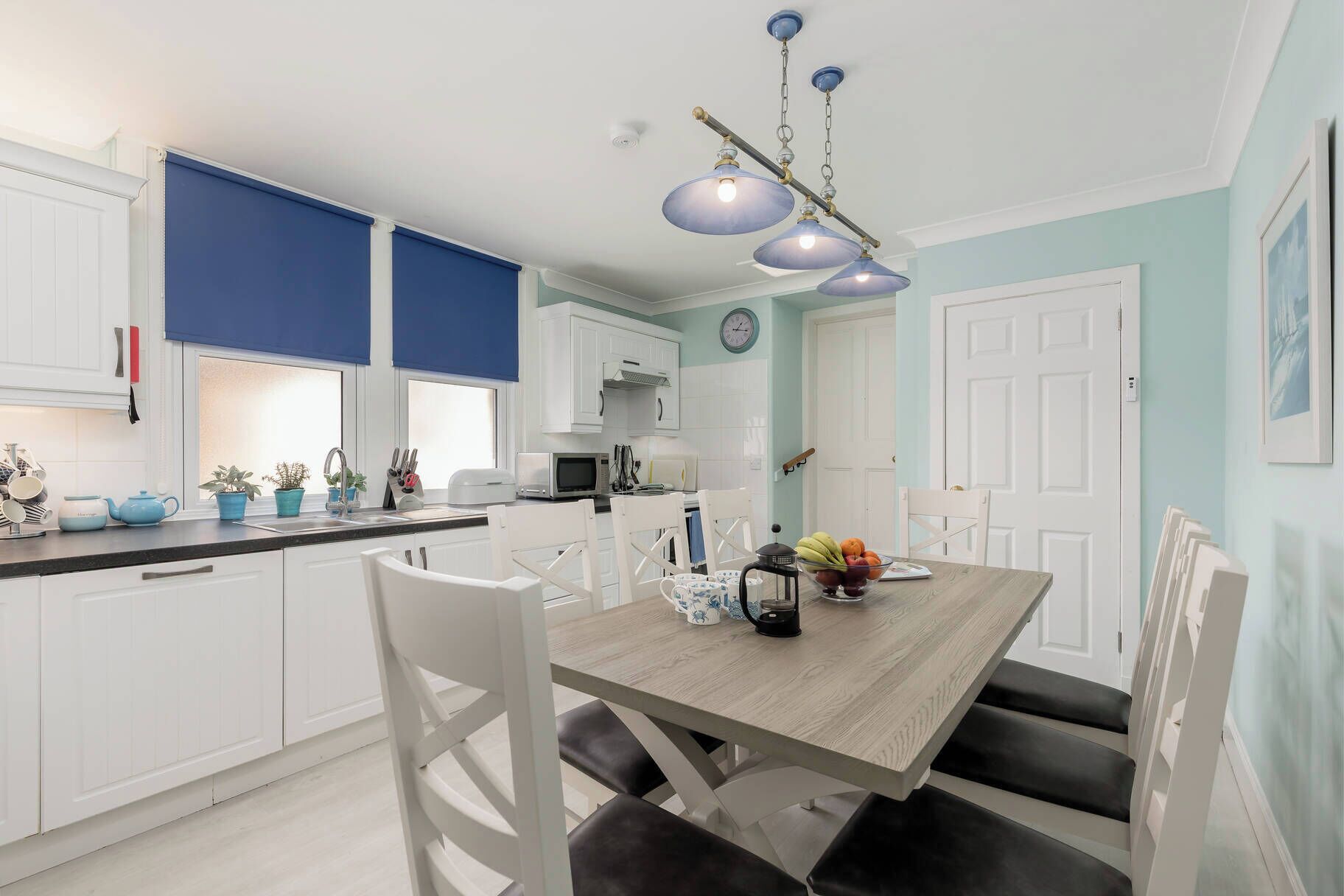Una cocina moderna con armarios blancos, una mesa de comedor de madera y detalles en azul.