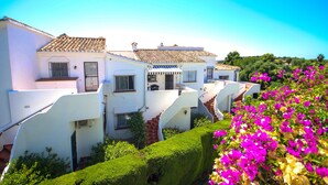 Eine weiße Villa mit Ziegeldach, einer Treppe und einem gepflegten Garten mit rosa Blüten.