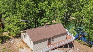 Una casa a un piano con veranda, circondata da alberi e da uno specchio d'acqua.