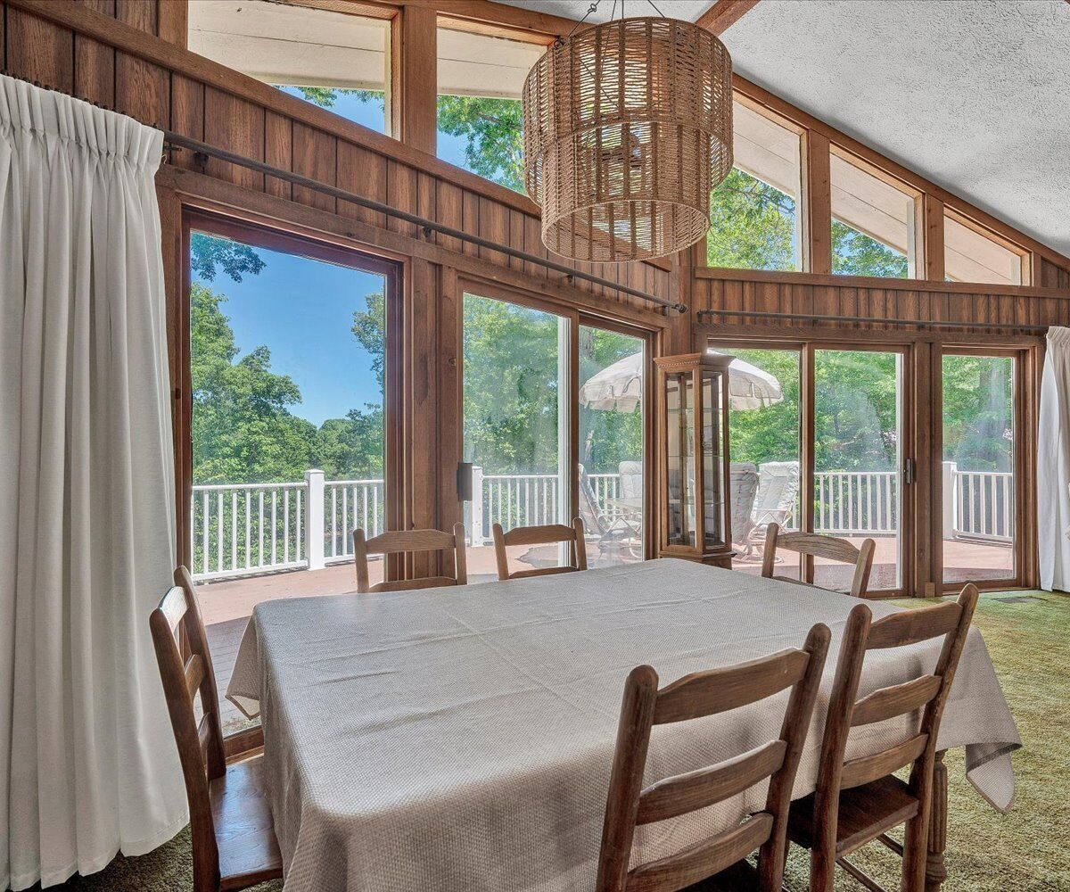 A dining area with a table and chairs, large windows, and a view of the outdoors.