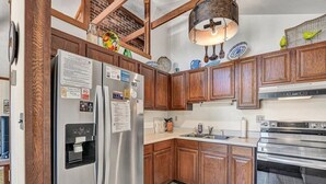 Una cucina con mobili in legno, un frigorifero in acciaio inossidabile, un forno integrato e una lampada a sospensione.