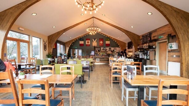 A restaurant with wooden tables and chairs, a bar area, and a high ceiling with wooden beams. - Base Camp Hotel Nevis Range (Fort William)